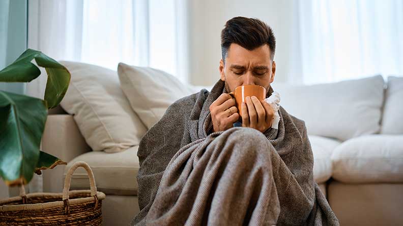 Mann trinkt Kräutertee gegen seine Grippebeschwerden.