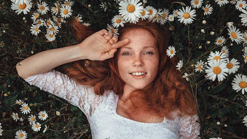 Eine junge hübsche Frau liegt in einer Wiese umgeben von großen Kamillenblumen